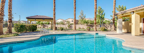 A swimming pool surrounded by palm trees and a building in the background.