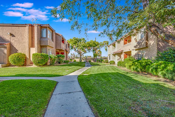 a walkway between two apartment buildings with grass and trees