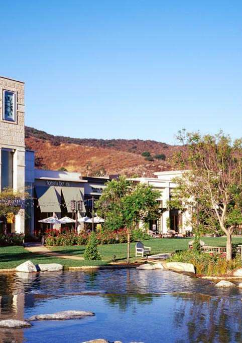 A building with a clock tower is surrounded by a pond and greenery.
