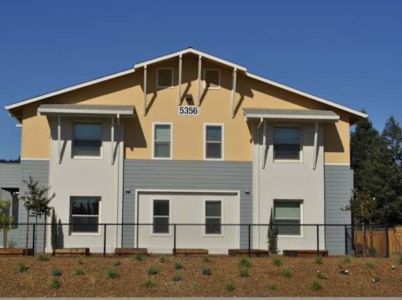 A two-story house with a grey and beige exterior and a black fence in front.