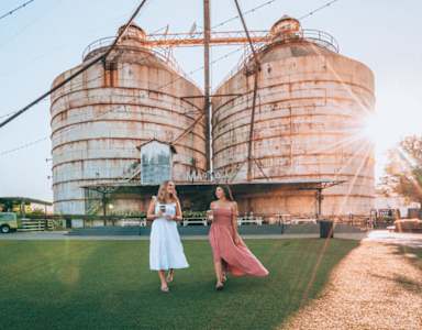 Two women walking in front of large silos.