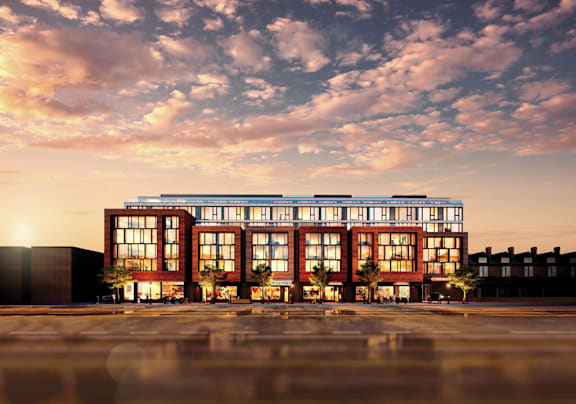 A modern building with large windows is illuminated from within, set against a twilight sky.