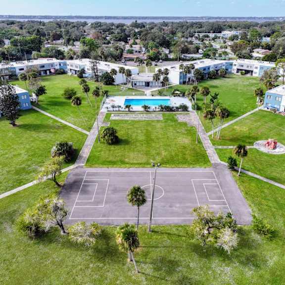A tennis court is surrounded by a grassy area and a pool.