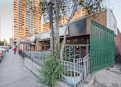 Thumbnail 6 of 8 - A tree in a planter is in front of a building with a green gate.