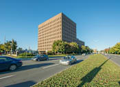Thumbnail 9 of 9 - A large building is situated on a street with cars driving by.