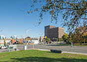 Thumbnail 7 of 9 - A city street with a large building in the background and a grassy area in the foreground.