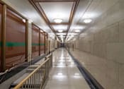 Thumbnail 4 of 7 - A long hallway with a metal railing on the left side and a marble floor.