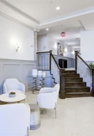 a lobby with white chairs and a staircase in the background