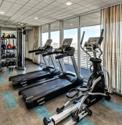 a gym with plenty of exercise equipment and a window view of the beach