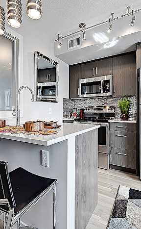 A modern kitchen with a stainless steel refrigerator, a white countertop, and black barstools.