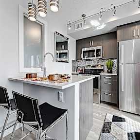 A modern kitchen with a stainless steel refrigerator, a white countertop, and black barstools.