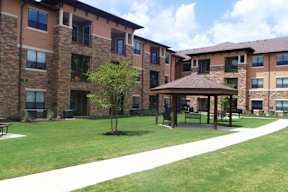 A tree is planted in a black pot in the lawn of a building.