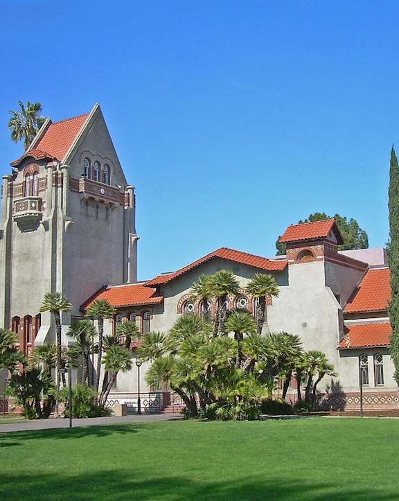 A large building with a tower and a red roof is surrounded by trees.