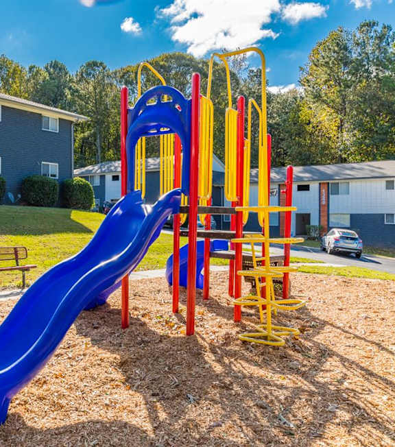 A playground with a blue metal structure and red chairs. at Balfour East Lake Apartments, New York, 30316