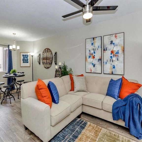 A living room with a beige couch, a ceiling fan, and a dining table with chairs.