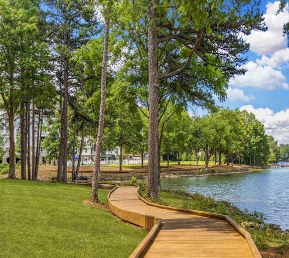 A wooden walkway runs along the edge of a lake, bordered by trees.