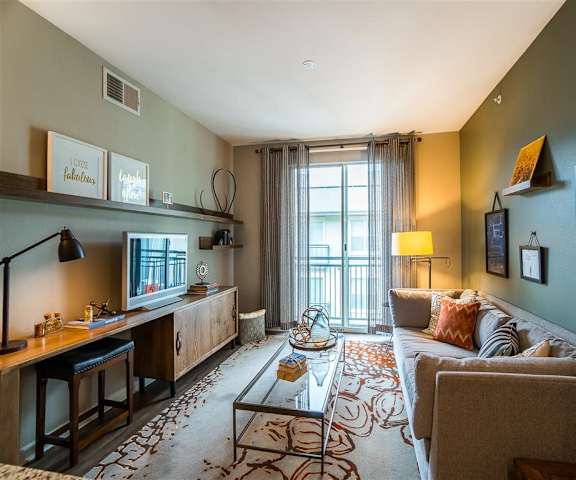 The living room with a couch, coffee table, decorations, a TV, and balcony at Parkside at Firewheel Apartments. 