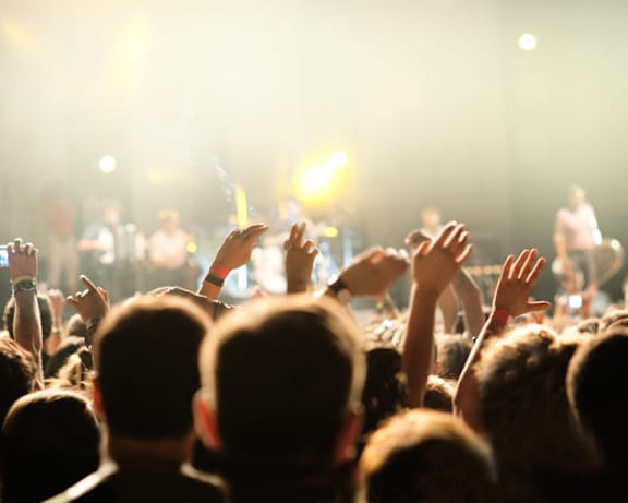 A crowd of people at a concert with their hands raised in the air.