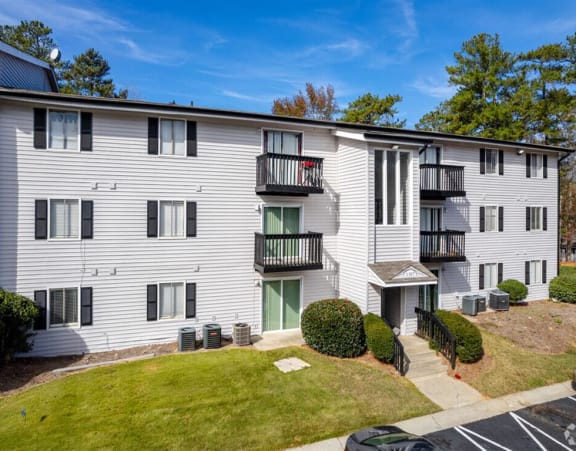 an apartment building with white siding and green grass and trees at Tucker Square, Stone Mountain, GA