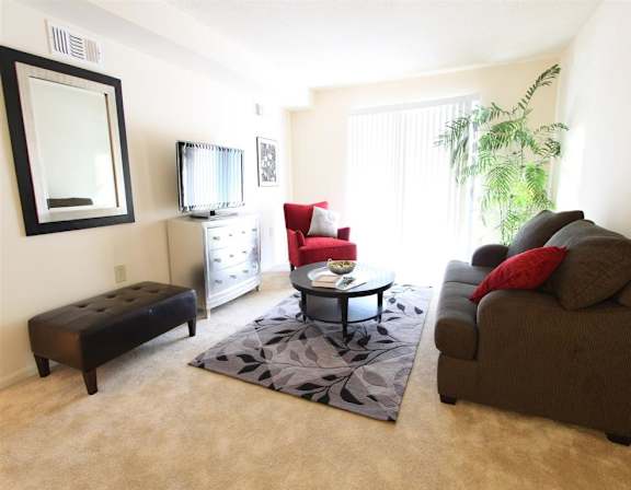 A living room with a brown couch, a red chair, and a black ottoman.
