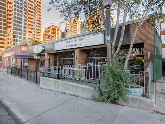 A building with a sign that says "For Guest Use, Visit" is located on a street with trees and other buildings in the background.