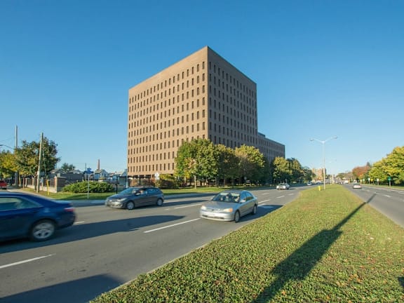 A large building is situated on a street with cars driving by.