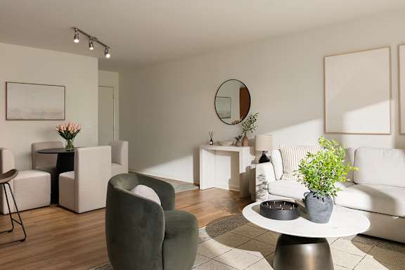 A living room with a white couch, a green chair, and a round mirror on the wall.