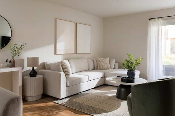 A living room with a white sofa, a grey armchair, and a round mirror on the wall.