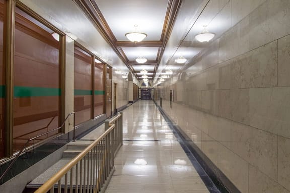 A long hallway with a metal railing on the left side and a marble floor.