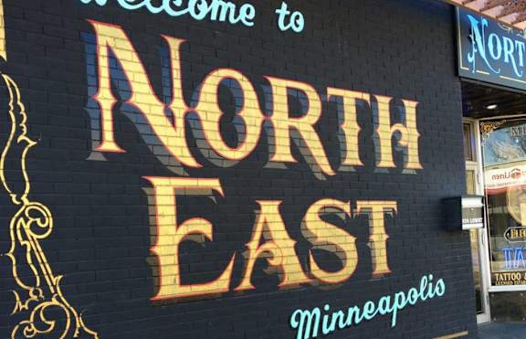 A sign that says "Welcome to North East Minneapolis" is displayed.
