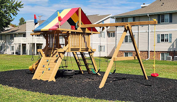 A wooden swing set with a red ball on the ground.