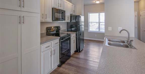 A room with a black fridge and wooden flooring.