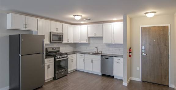 A room with a black fridge and wooden flooring.