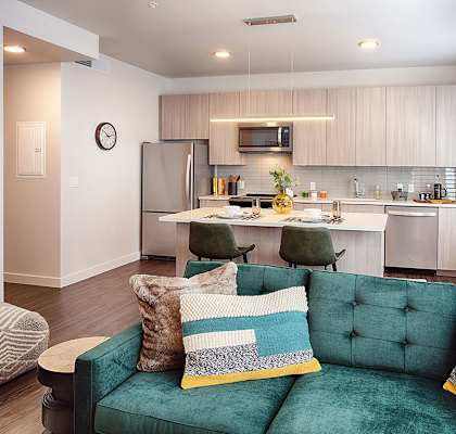 a living room with a green couch and a kitchen in the background