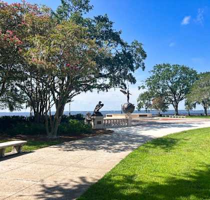 a park with trees and a statue in front of the water