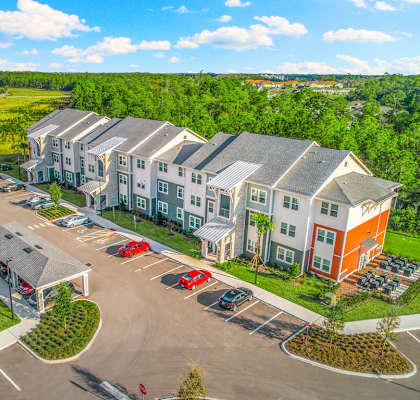a large apartment complex with a parking lot and a green field in the background