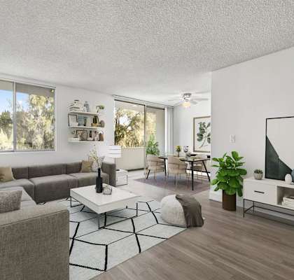A living room with a grey couch, a white coffee table, and a large window with a view of trees.