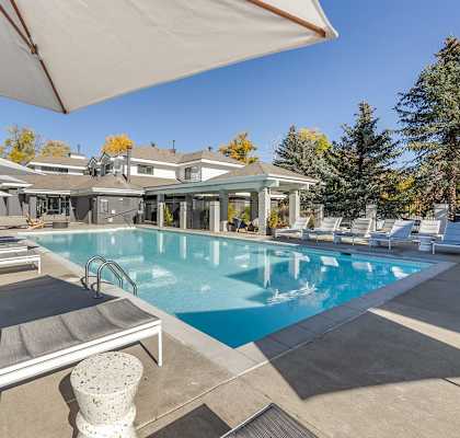 a swimming pool with chairs and umbrellas in front of a house