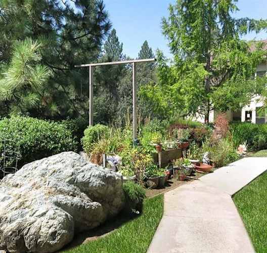a garden with a large rock and potted plants on a sidewalk at Hilltop Commons Senior Living, California