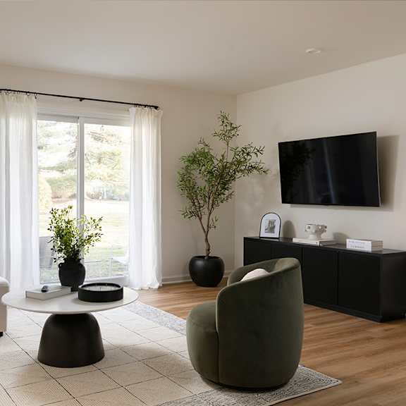 A living room with a green chair, a white sofa, a black table, and a flat screen TV mounted on the wall.