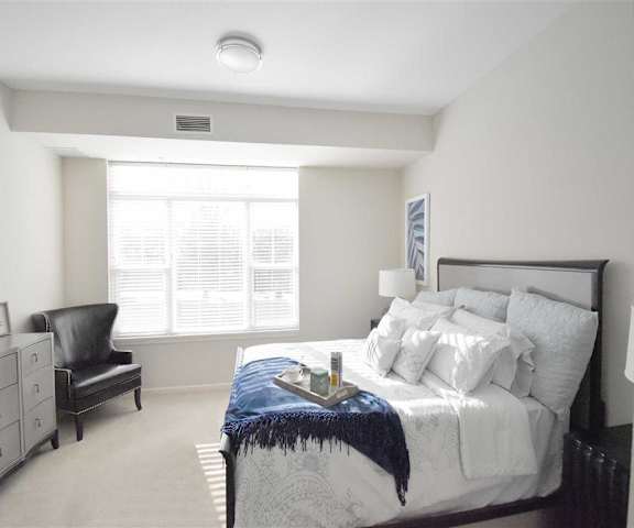 A bedroom with a queen-size bed, a dresser, decorations, window, and nightstands at Oaks of Shorewood Apartments.  