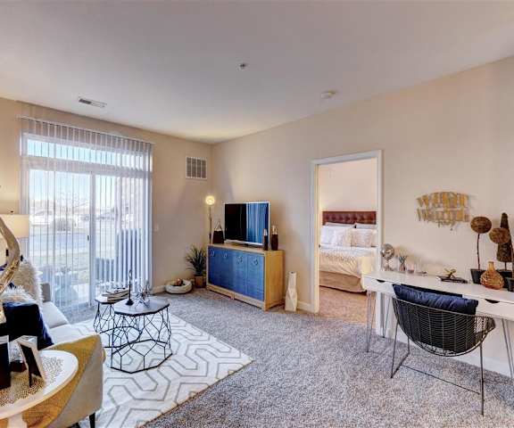 The living room with a couch, plush chairs, coffee table, decorations, natural lighting, a TV, and balcony at Residence at North Penn Apartment Homes. 