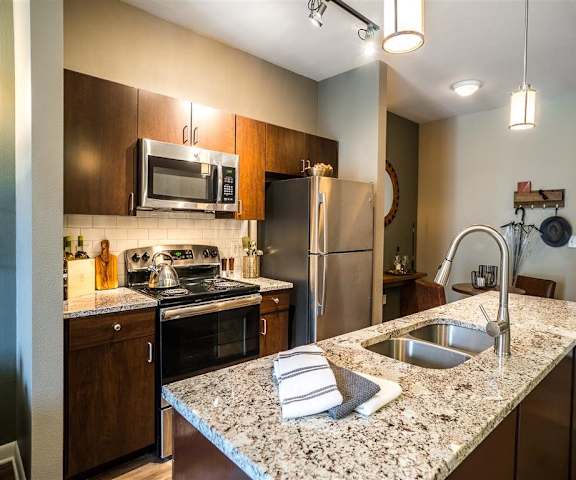 A kitchen with stainless steel appliances and wooden cabinets at Parkside at Firewheel Apartments. 