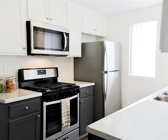 A kitchen with stainless steel and black appliances, marble countertops, and large white wooden cabinets at Hillside Village. 