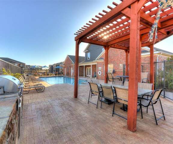 The community pool area, with a turquoise pool, pool chairs, and grill area, with a grill and outdoor dining table and chairs at Residence at North Penn Apartment Homes. 