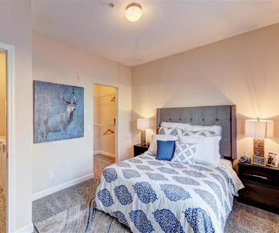 A cozy bedroom with a queen-size bed with blue and white bedding, a dresser, decorations, a painting with an elk, a closet, and nightstands at Residence at North Penn Apartment Homes. 