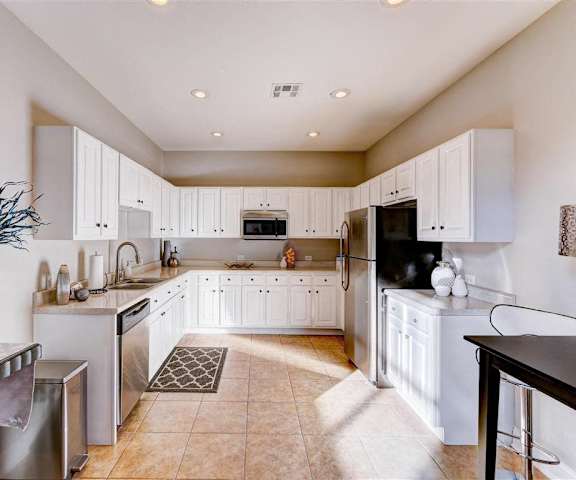 A large kitchen with stainless steel appliances, vases, spacious marble countertops, and large white wooden cabinets at Residence at North Penn Apartment Homes. 