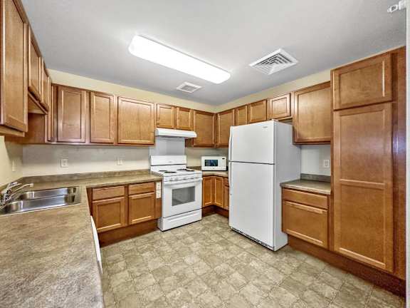 A kitchen with white appliances and wooden cabinets.at Cornerstone Commons, Iowa, 50131