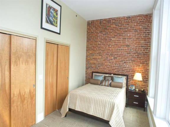 A bedroom with a bed, nightstand, and two doors at The Granite Works Apartments , Buffalo, NY