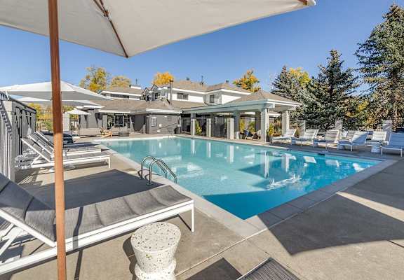 a swimming pool with chairs and umbrellas in front of a house